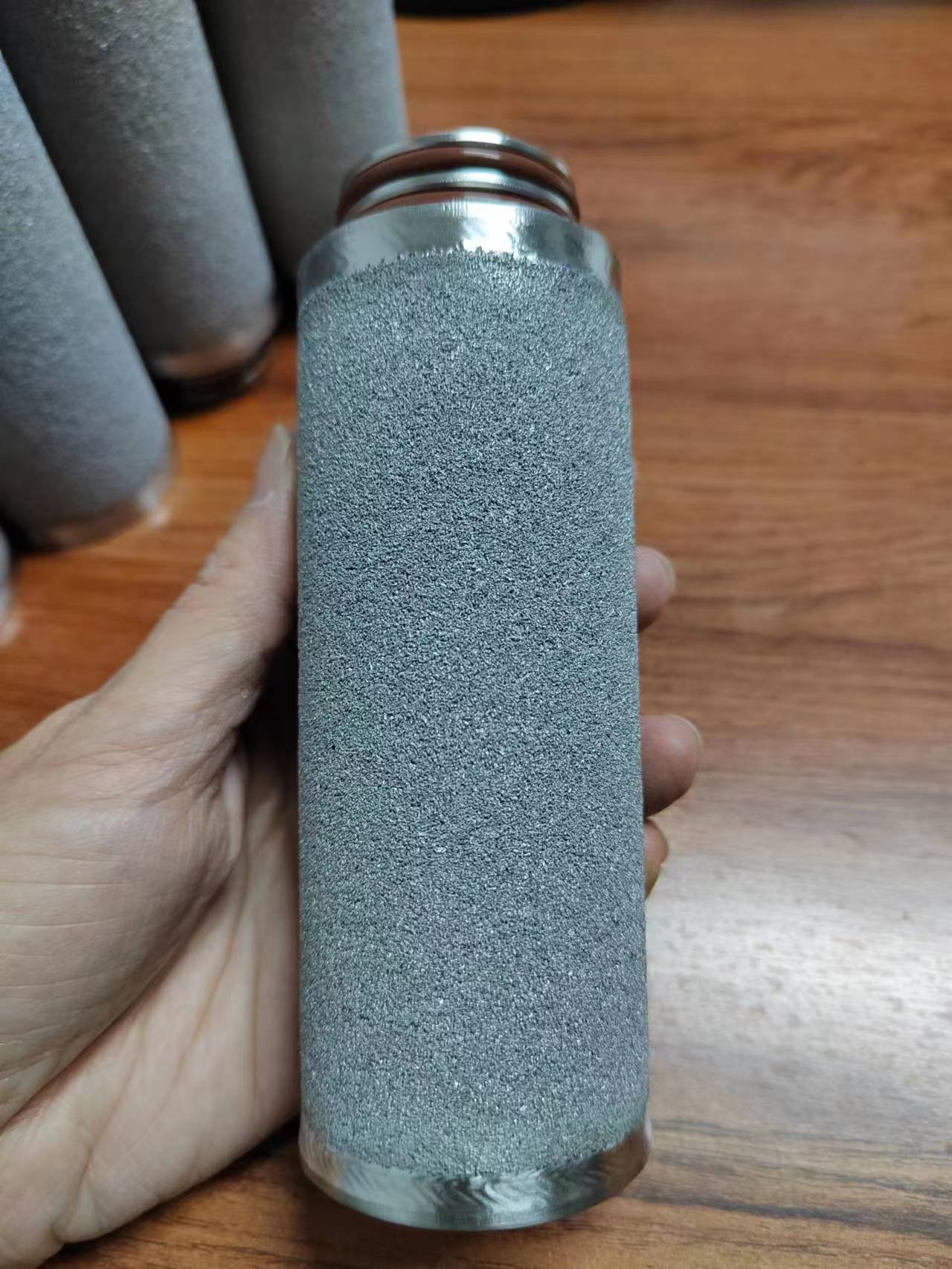 Hand holding a powder-sintered porous metal cylinder with a metal connector