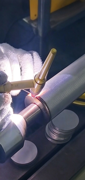Worker joining a cylindrical metal mesh component at the seam
