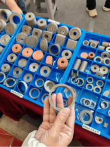 A hand holding a compressed knitted wire mesh ring in front of blue sample trays