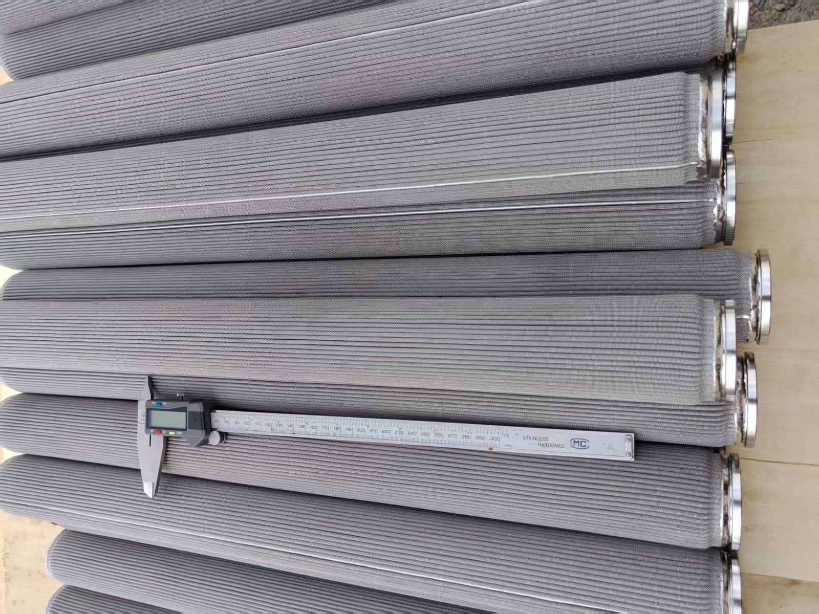 Stainless steel pleated wire mesh filter cartridges beside a digital caliper