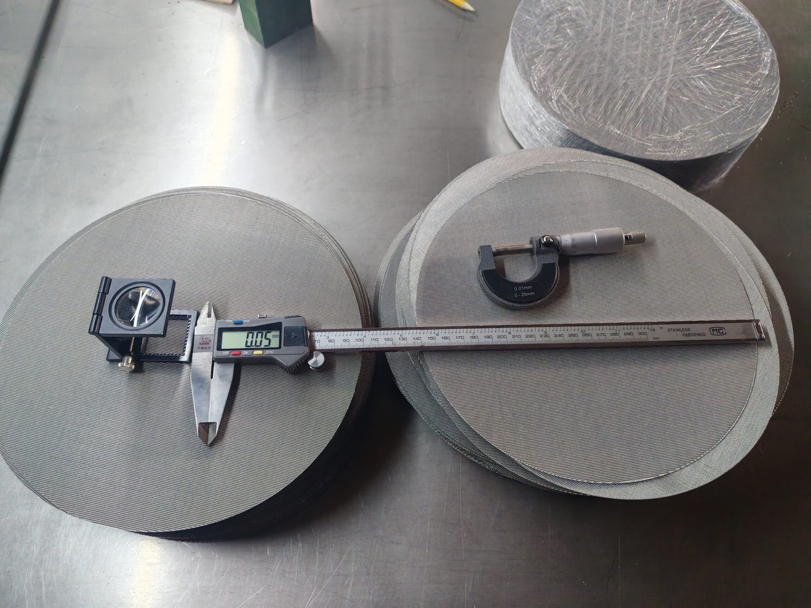 Mesh discs with a folding magnifier, digital caliper and micrometer on a work surface